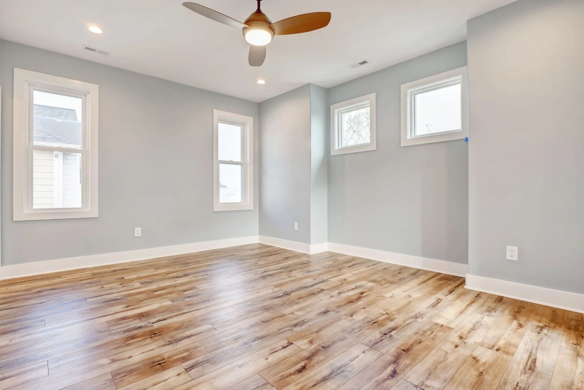 Empty bedroom with light blue walls, hardwood floor, and ceiling fan.