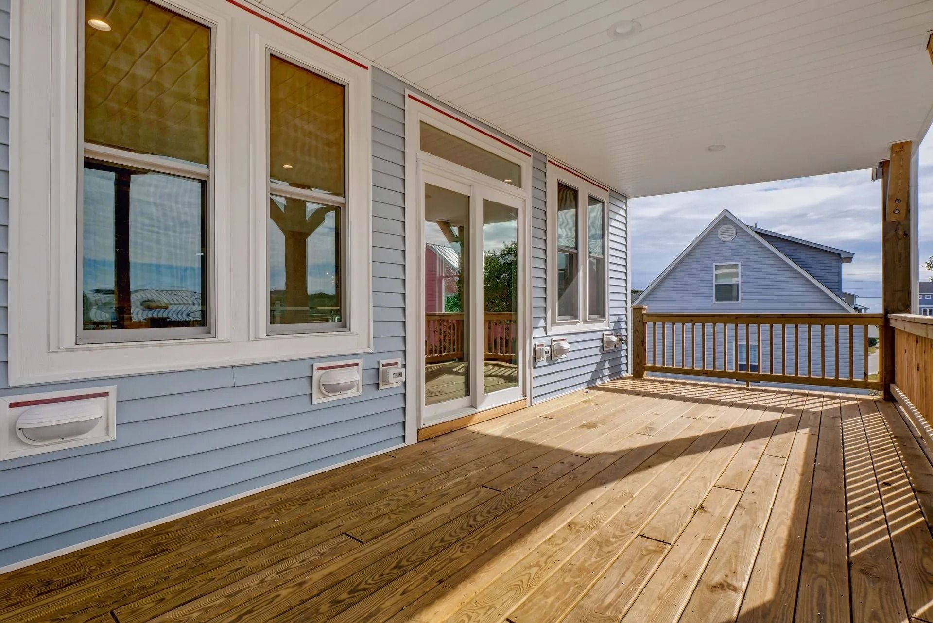 Covered porch with wood flooring, blue siding, windows, and a view of a neighboring house.