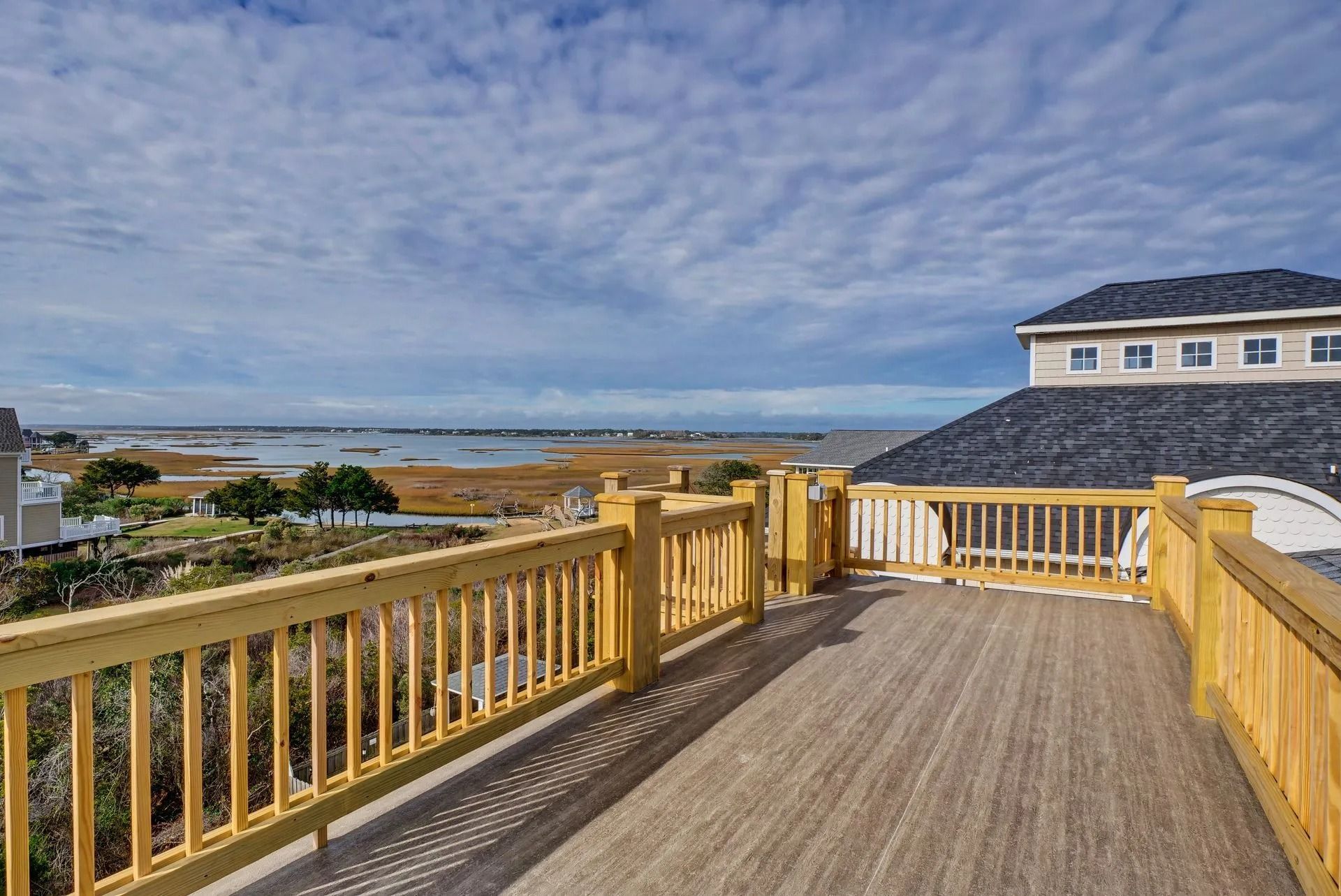 Wooden deck with yellow railing overlooking a marsh and ocean under a cloudy sky.