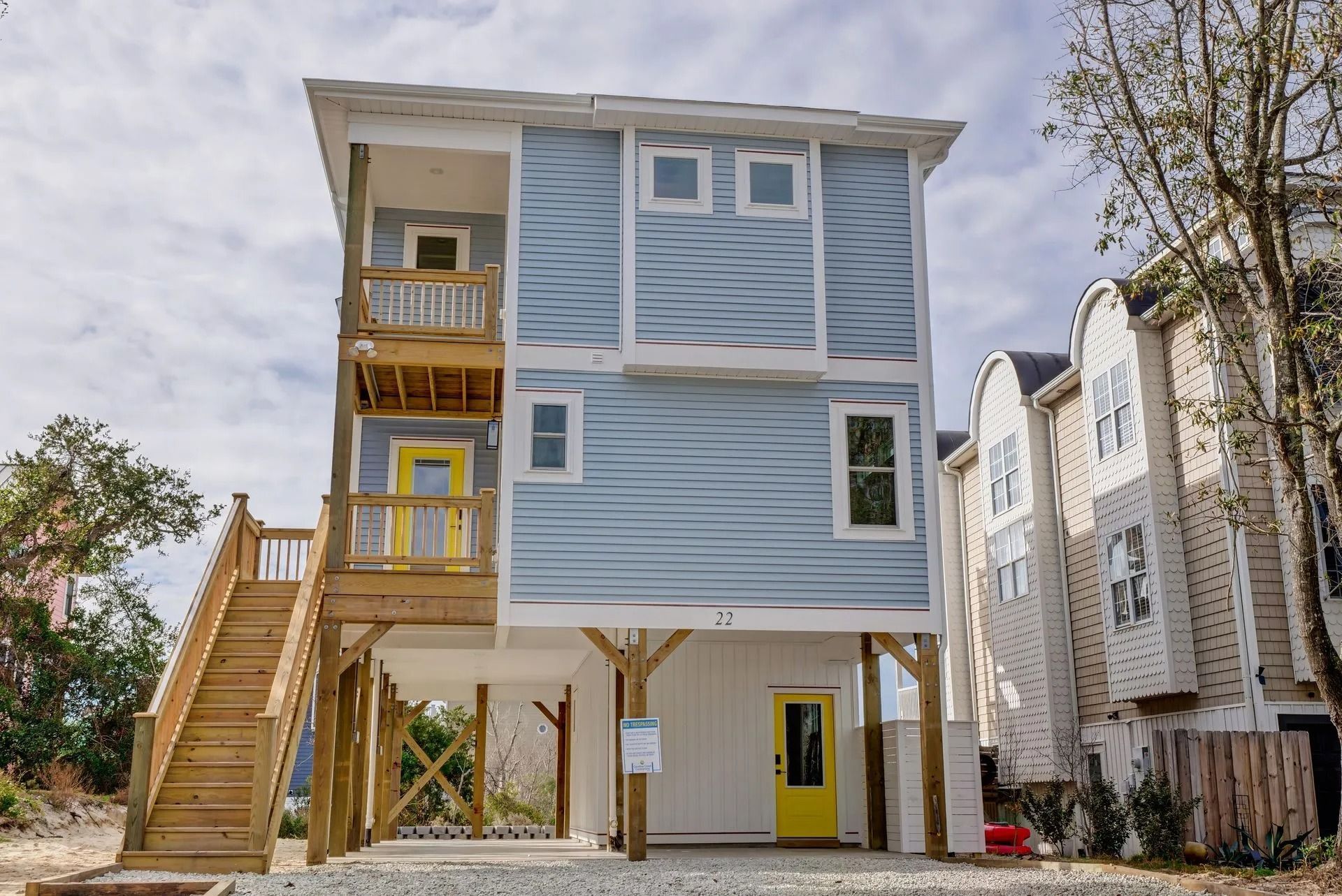 Three-story house with light blue siding, yellow doors, and wooden stairs.