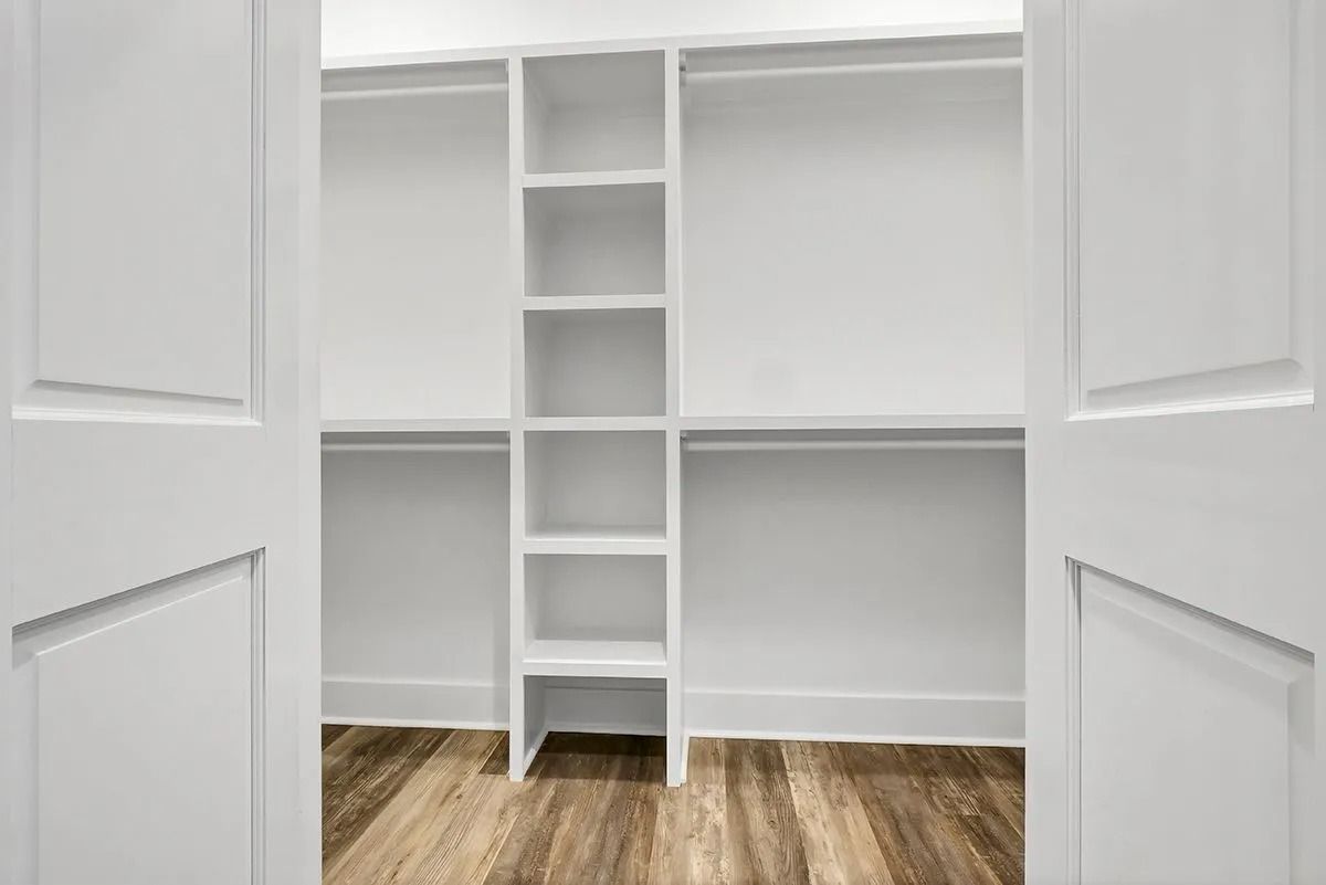 White empty closet with shelves, wood-look floor, and open white doors.