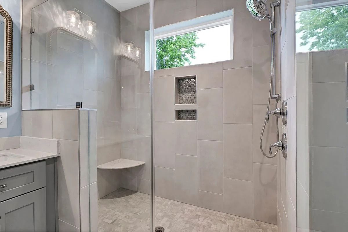 Modern bathroom with a glass shower enclosure, gray tiles, and a built-in shower seat.