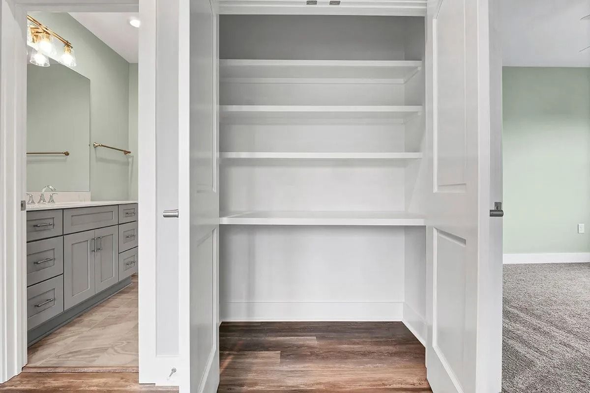 Empty white built-in shelves between a bathroom and a room with carpet.