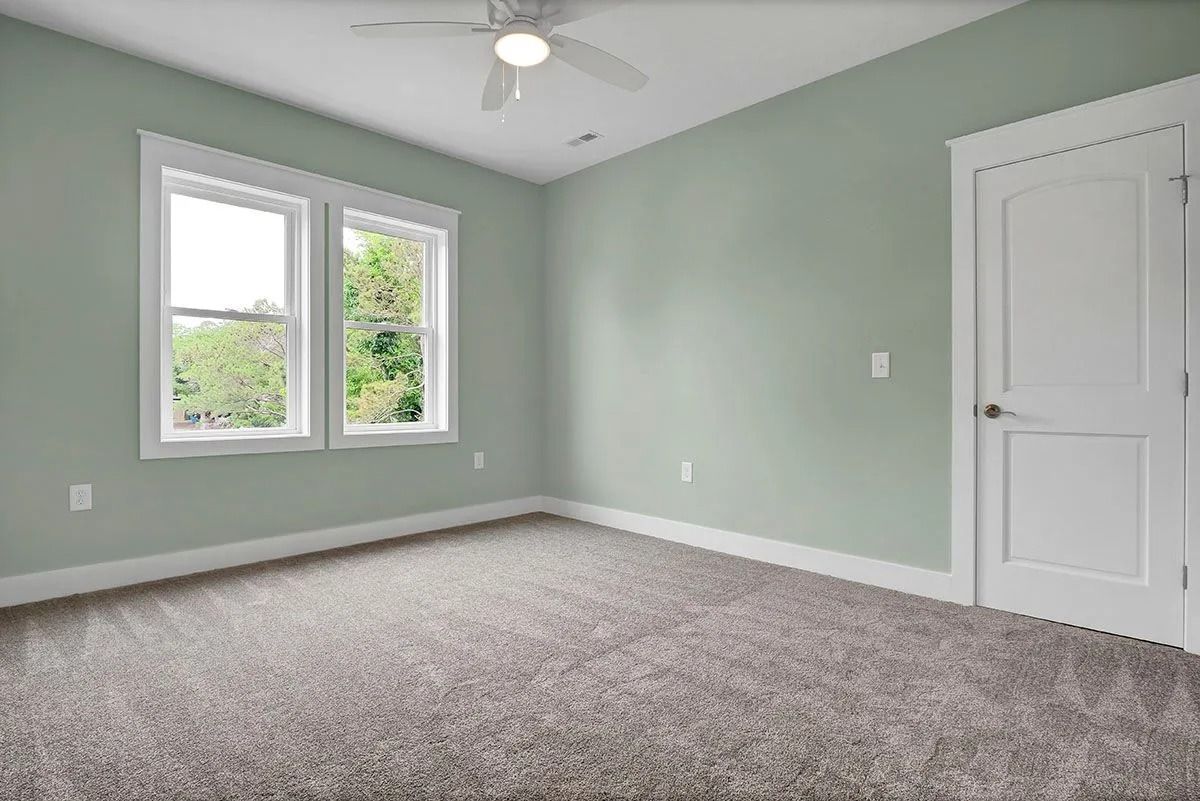 Empty room with mint green walls, white trim, two windows, door, and gray carpet.
