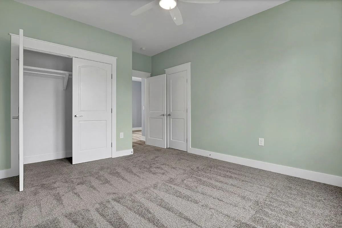 Empty bedroom with light green walls, white doors, and gray carpet.