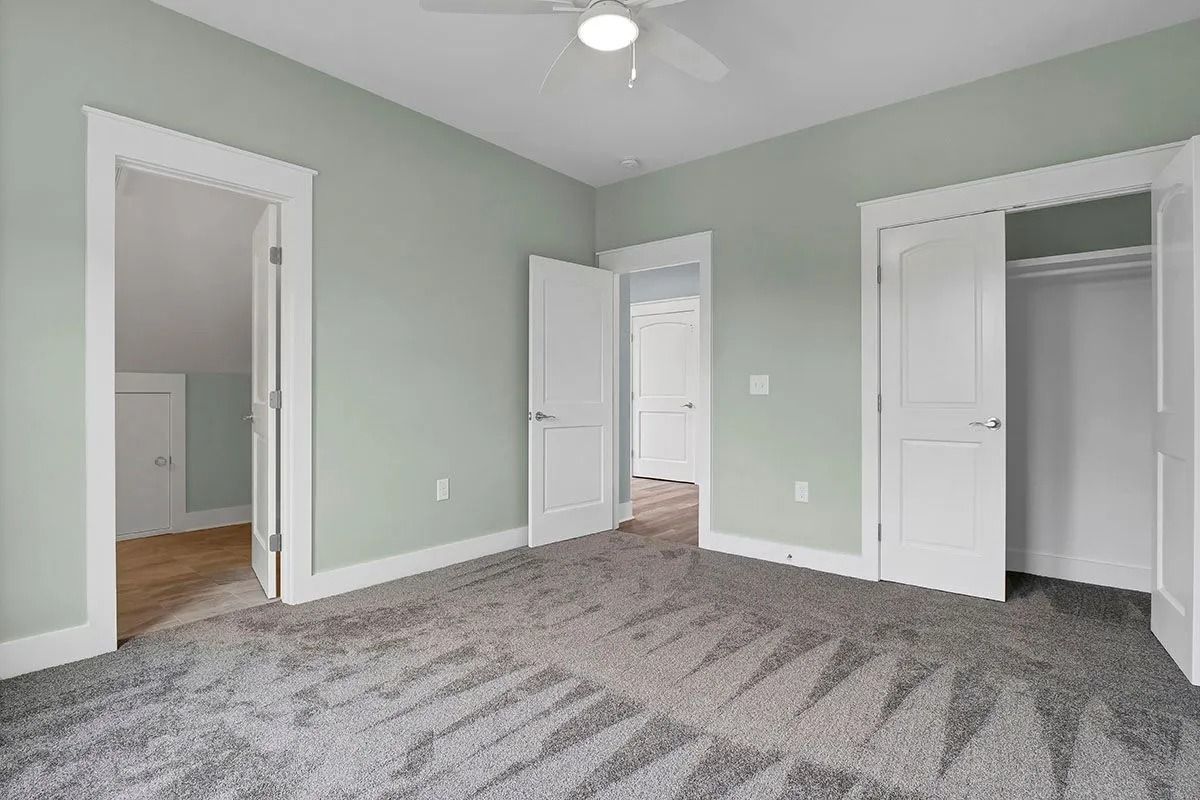 Empty bedroom with gray carpet, pale green walls, and white doors.