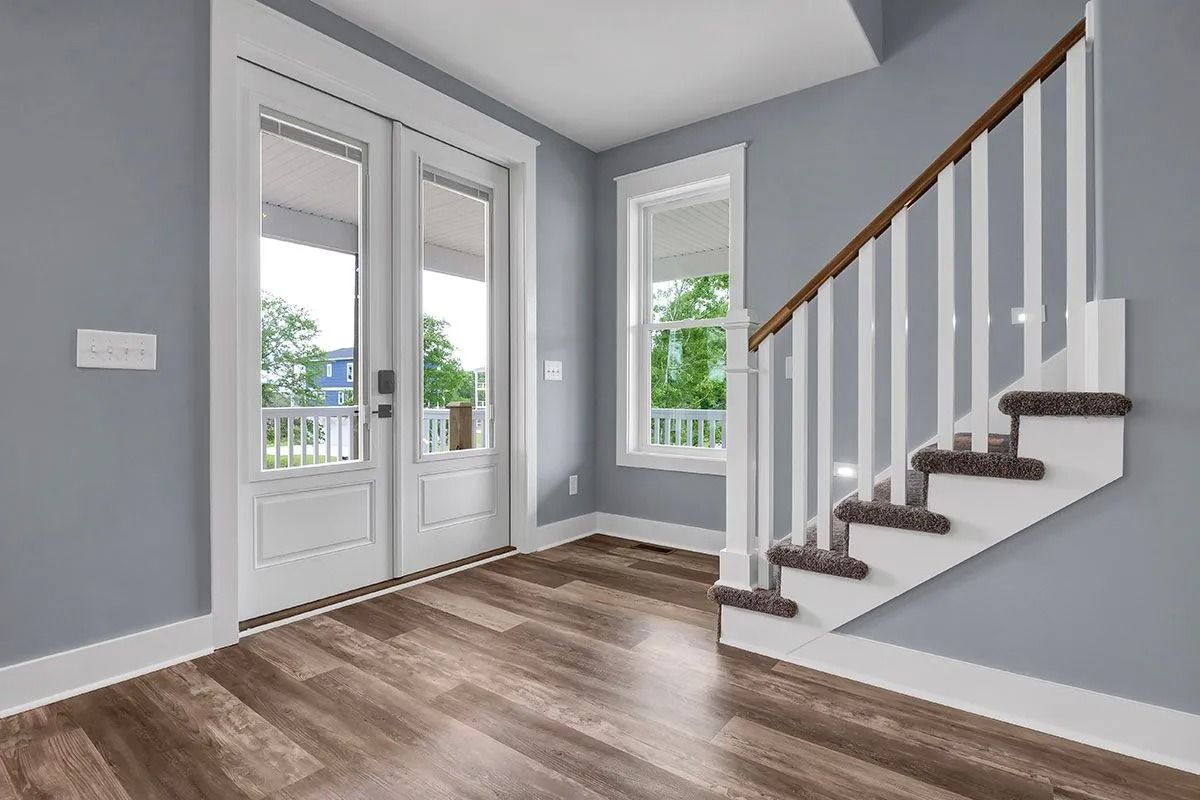 Entryway with wooden floor, stairs, French doors, and a window. Light blue walls, white trim.