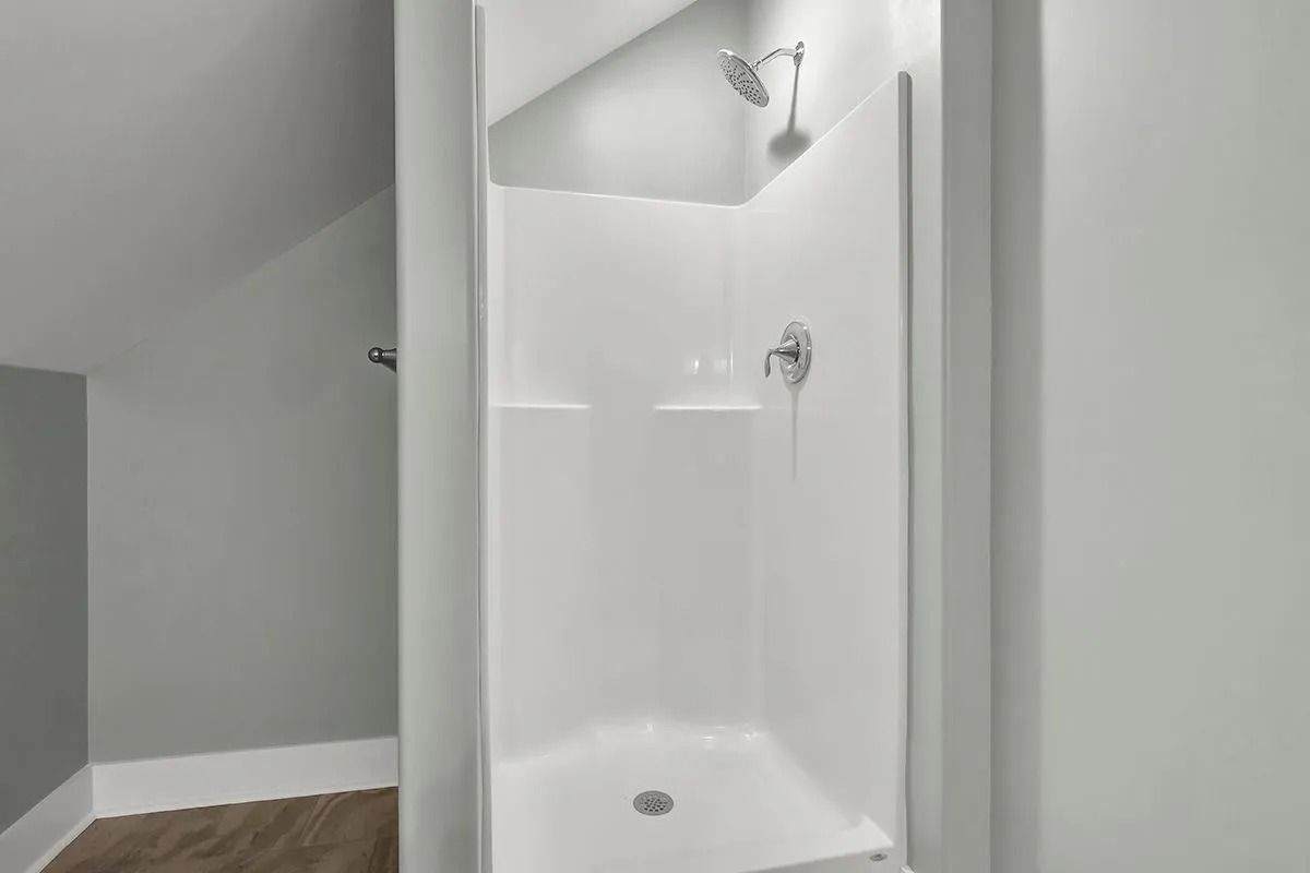 White shower stall in a bathroom with sloped ceiling and wood-look flooring.