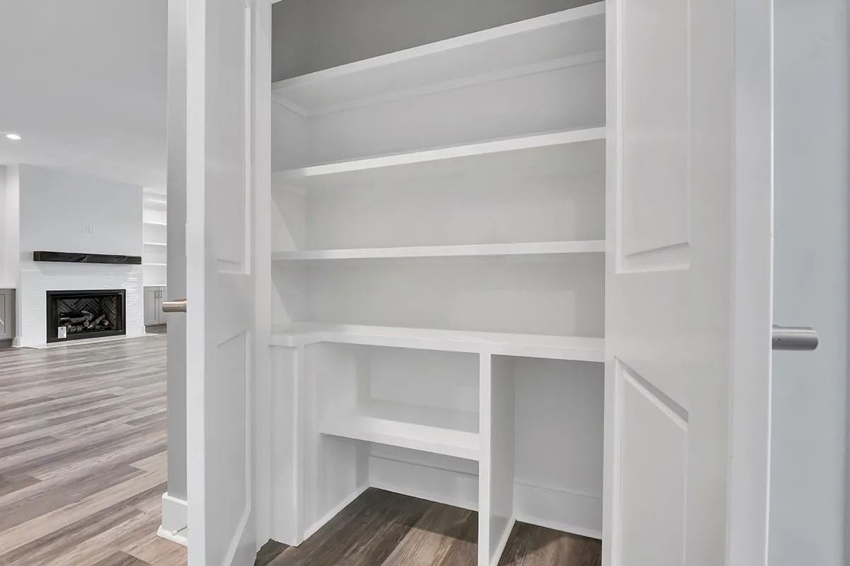 White built-in pantry with shelves, partially open. A living room with a fireplace is visible in the background.