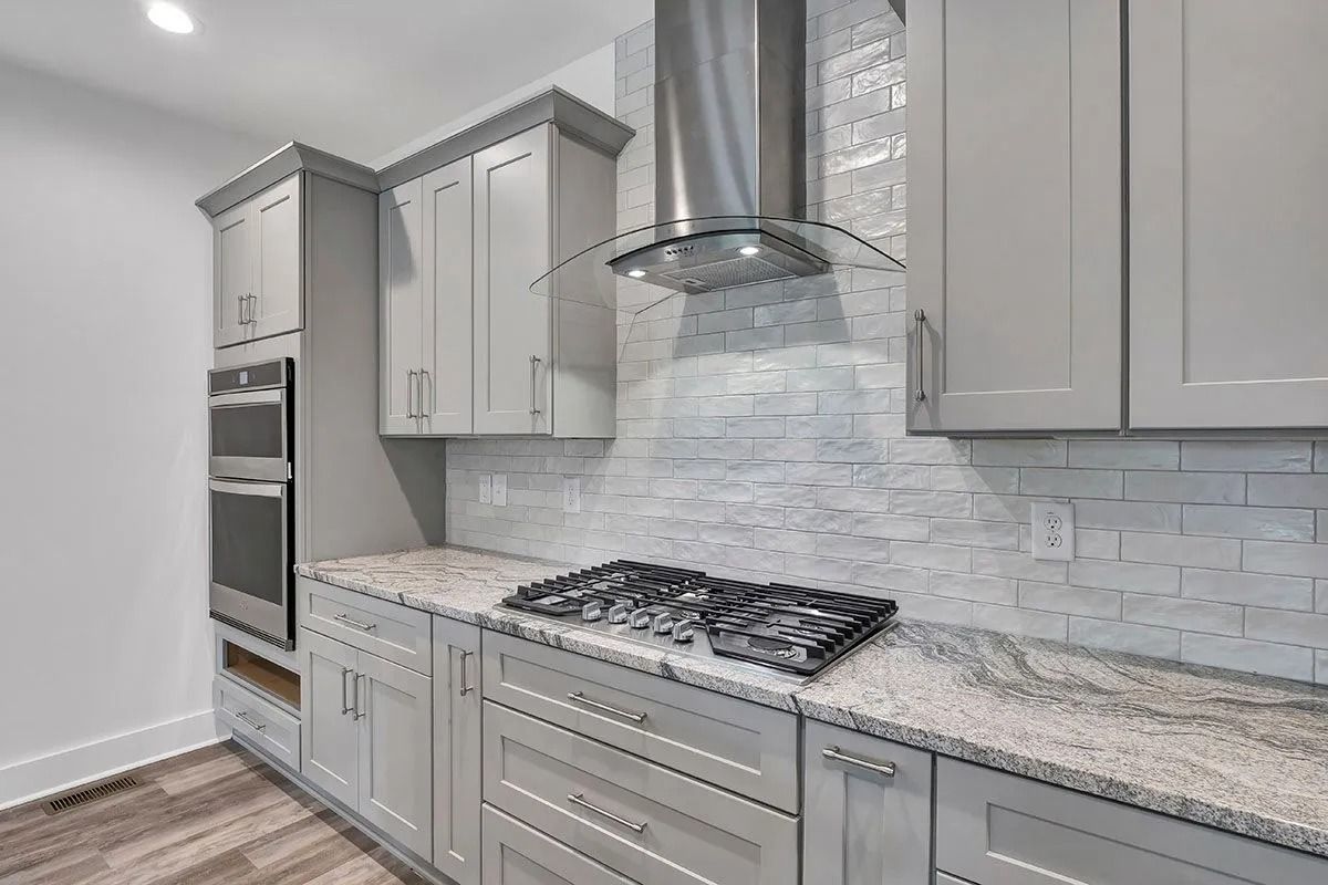 Gray kitchen with granite countertops, stainless steel range hood, and tile backsplash.