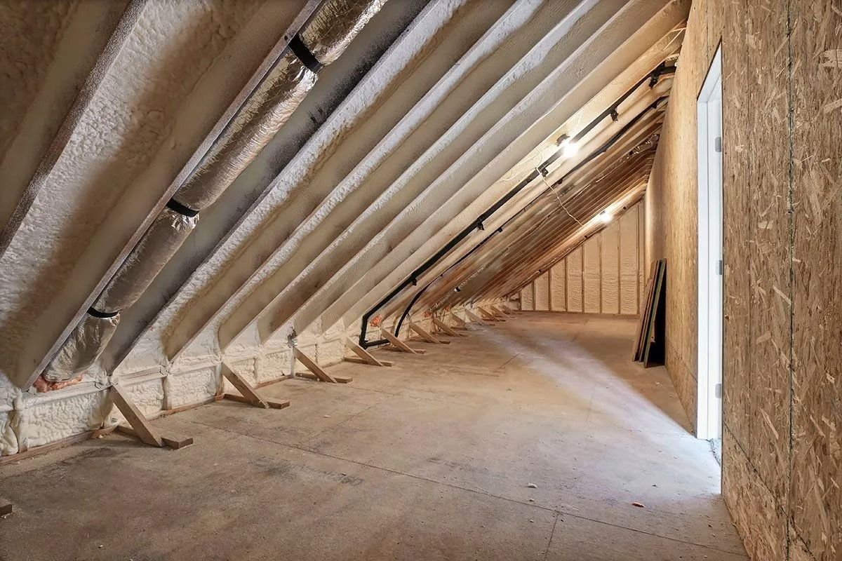 Attic space insulated with spray foam, diagonal wooden beams, and a small window.