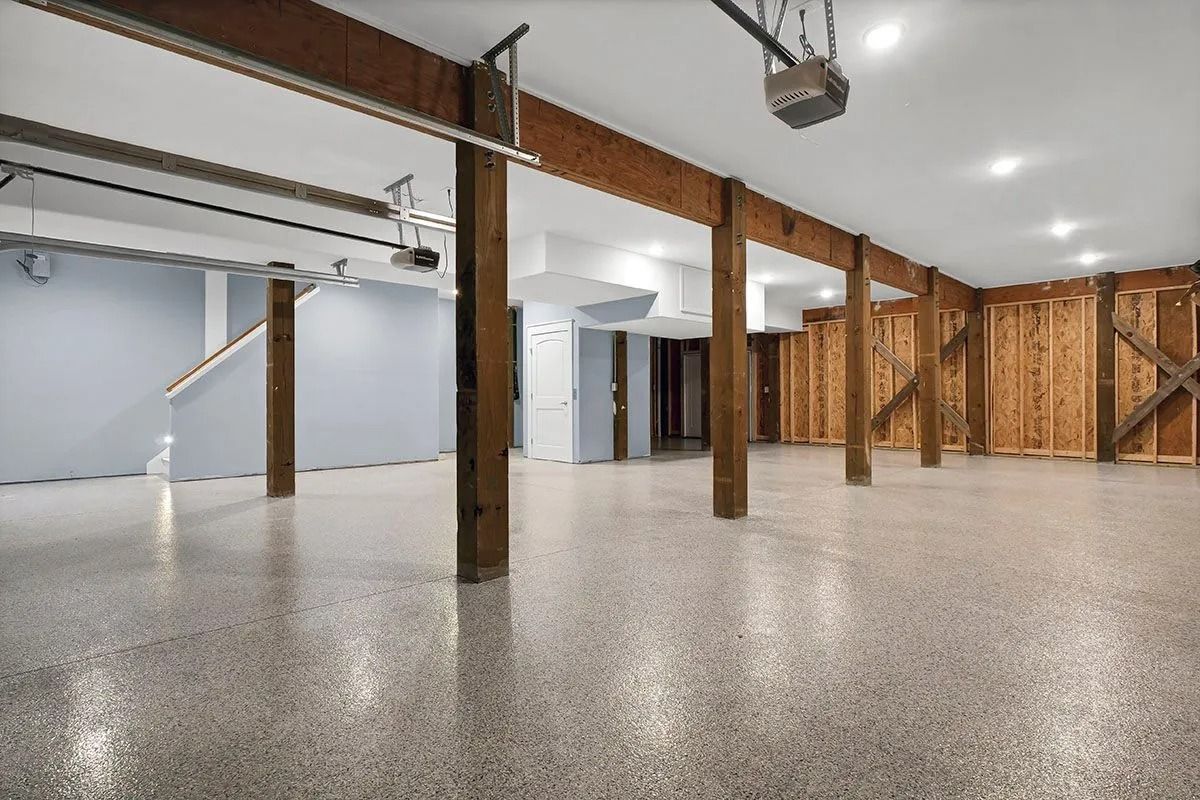 Empty, spacious garage with speckled flooring, wooden support beams, and exposed wood wall.
