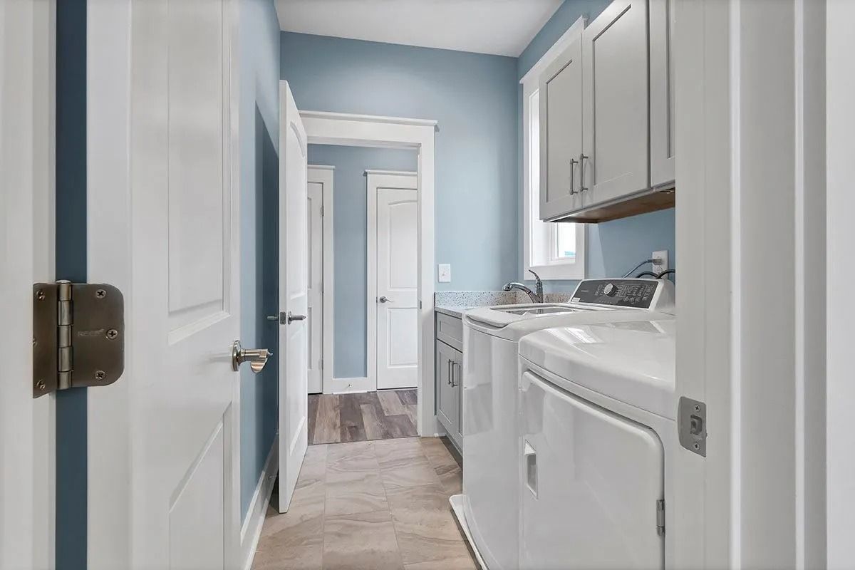 Laundry room with white appliances, cabinets, and blue walls.