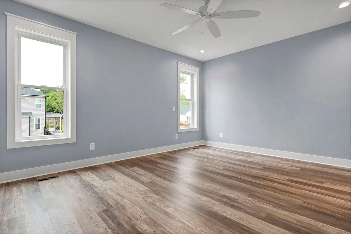 Empty bedroom with blue walls, two windows, wood floor, and ceiling fan.
