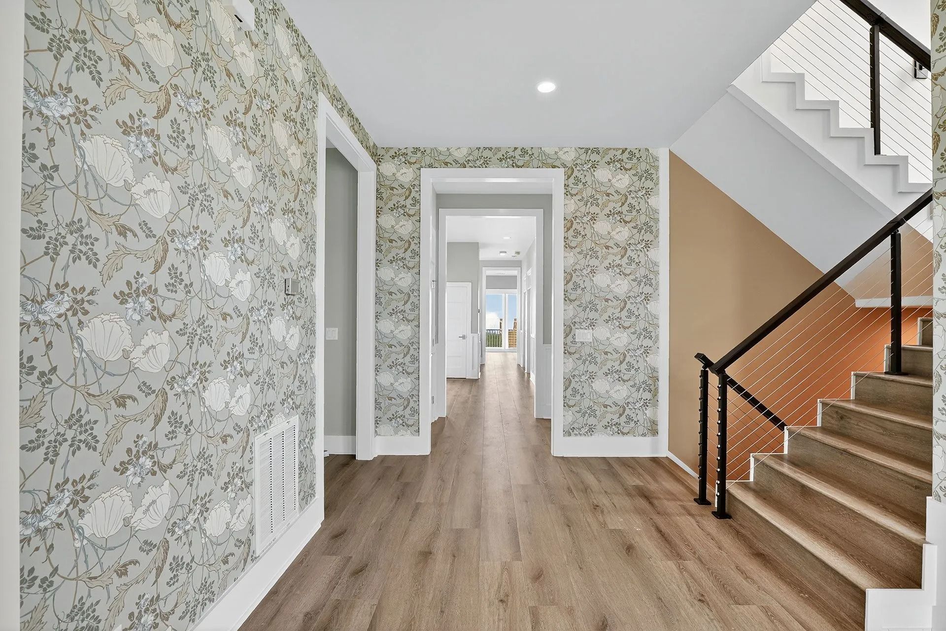 Hallway with floral wallpaper, wooden floor, and a staircase with a black railing.