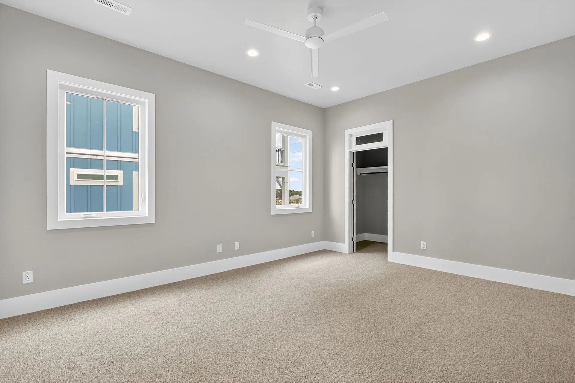 Empty bedroom with gray walls, white trim, two windows, closet, and beige carpet.