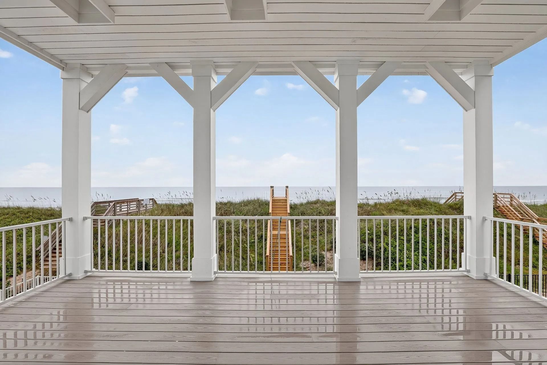 White porch with ocean view, railing, wooden floor, and structural beams.