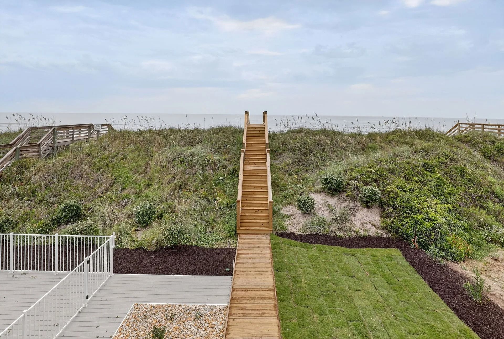 Wooden stairs lead up a grassy dune to the ocean on a cloudy day.