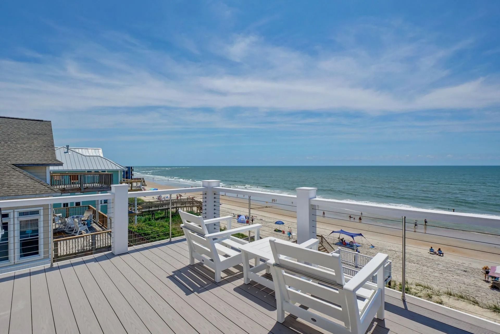 Oceanfront deck with white chairs, small table, and ocean view on a sunny day.