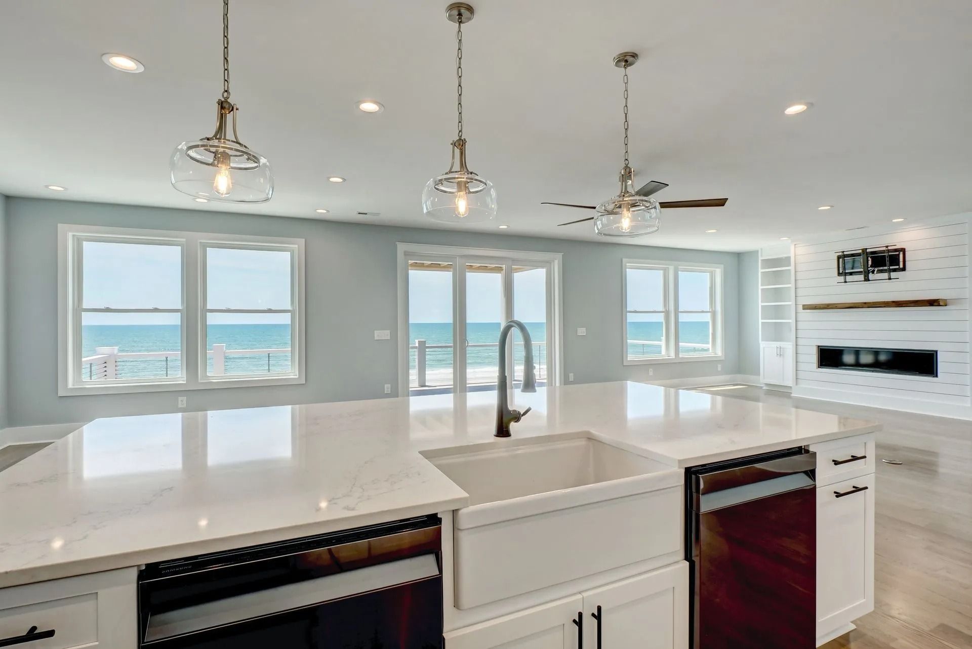 Modern kitchen with white island, farmhouse sink, ocean view, pendant lights.