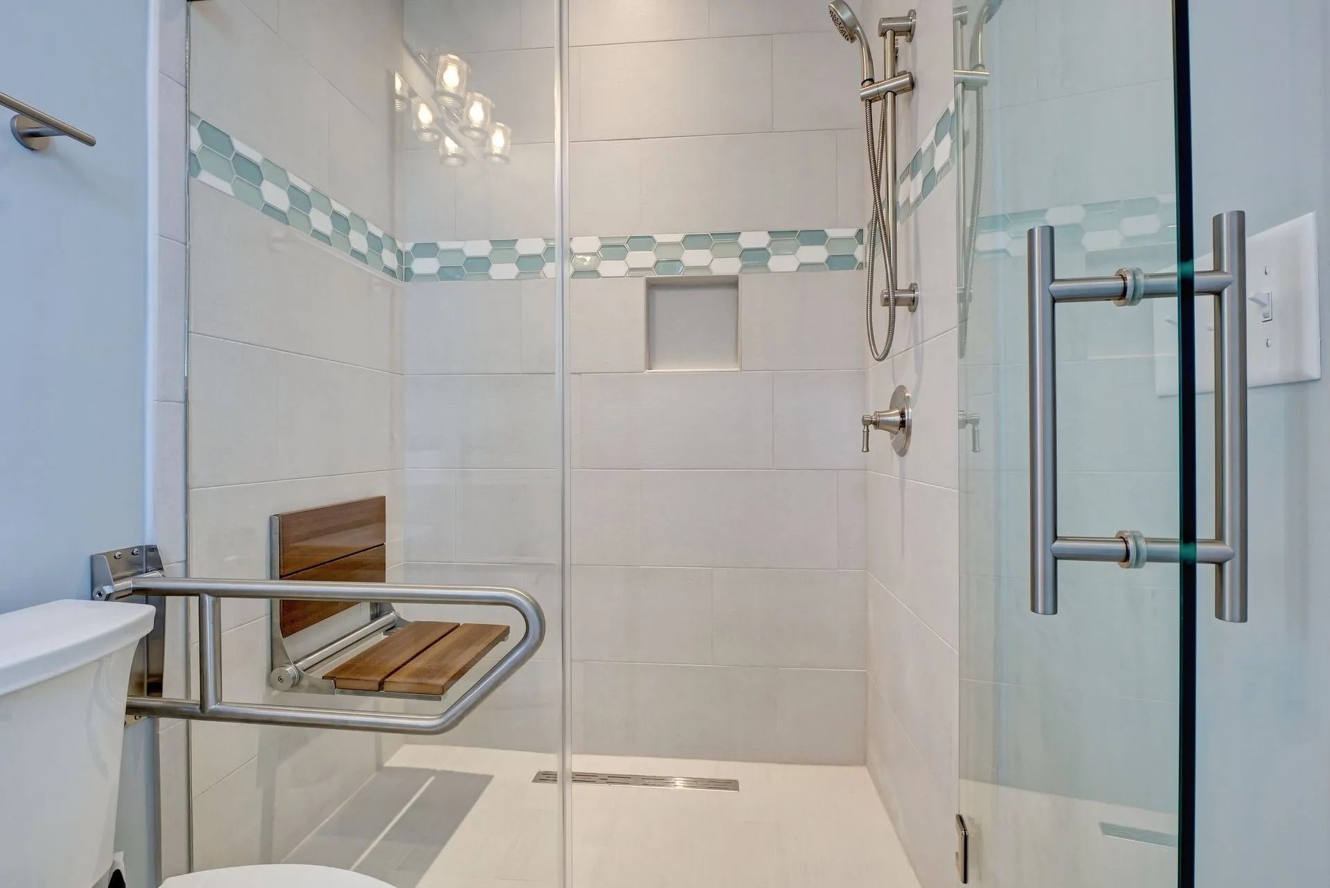 Accessible bathroom with glass shower door, grab bar, shower seat, and tile.