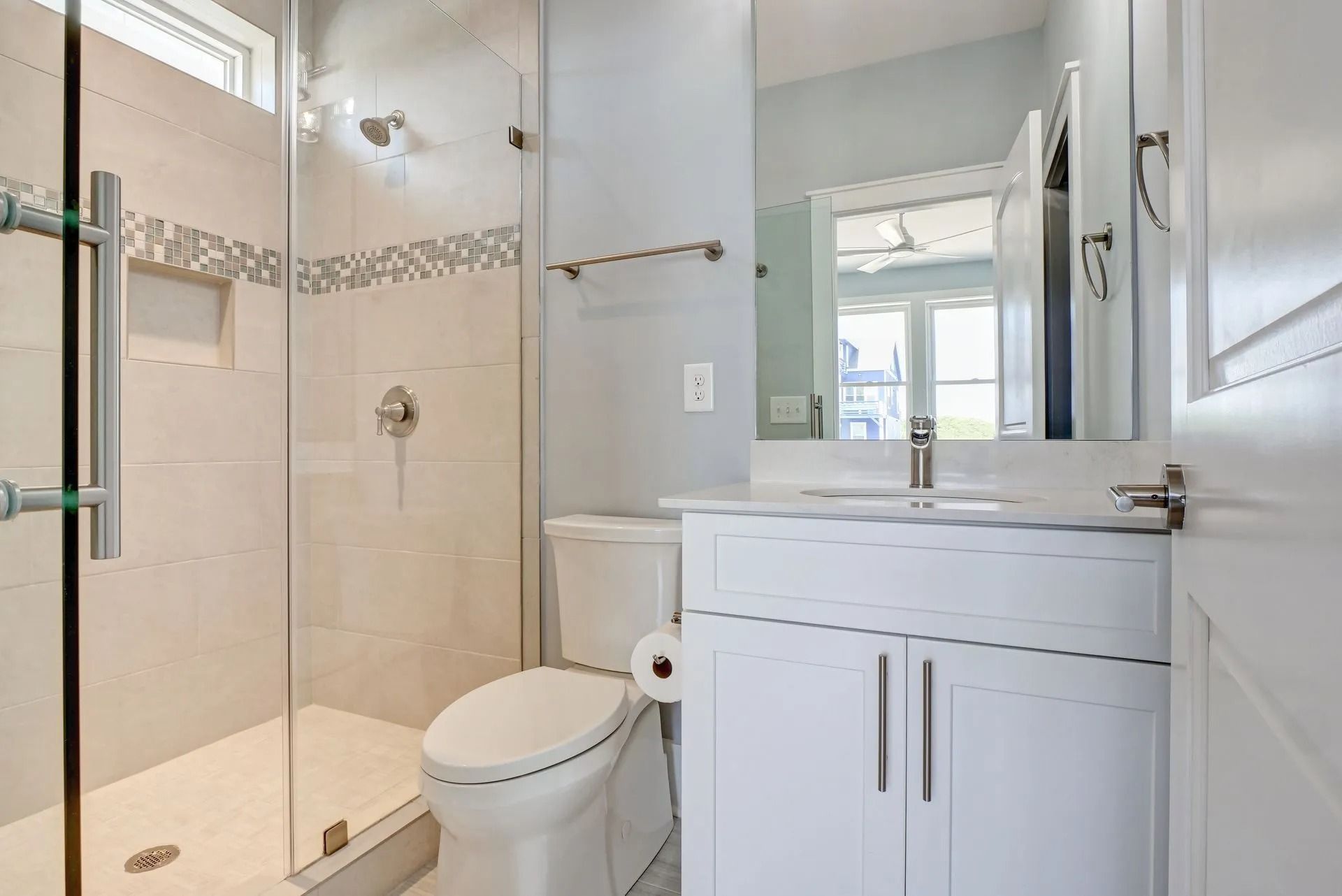 Bathroom with a white vanity, toilet, and glass shower. Light blue walls, chrome fixtures.