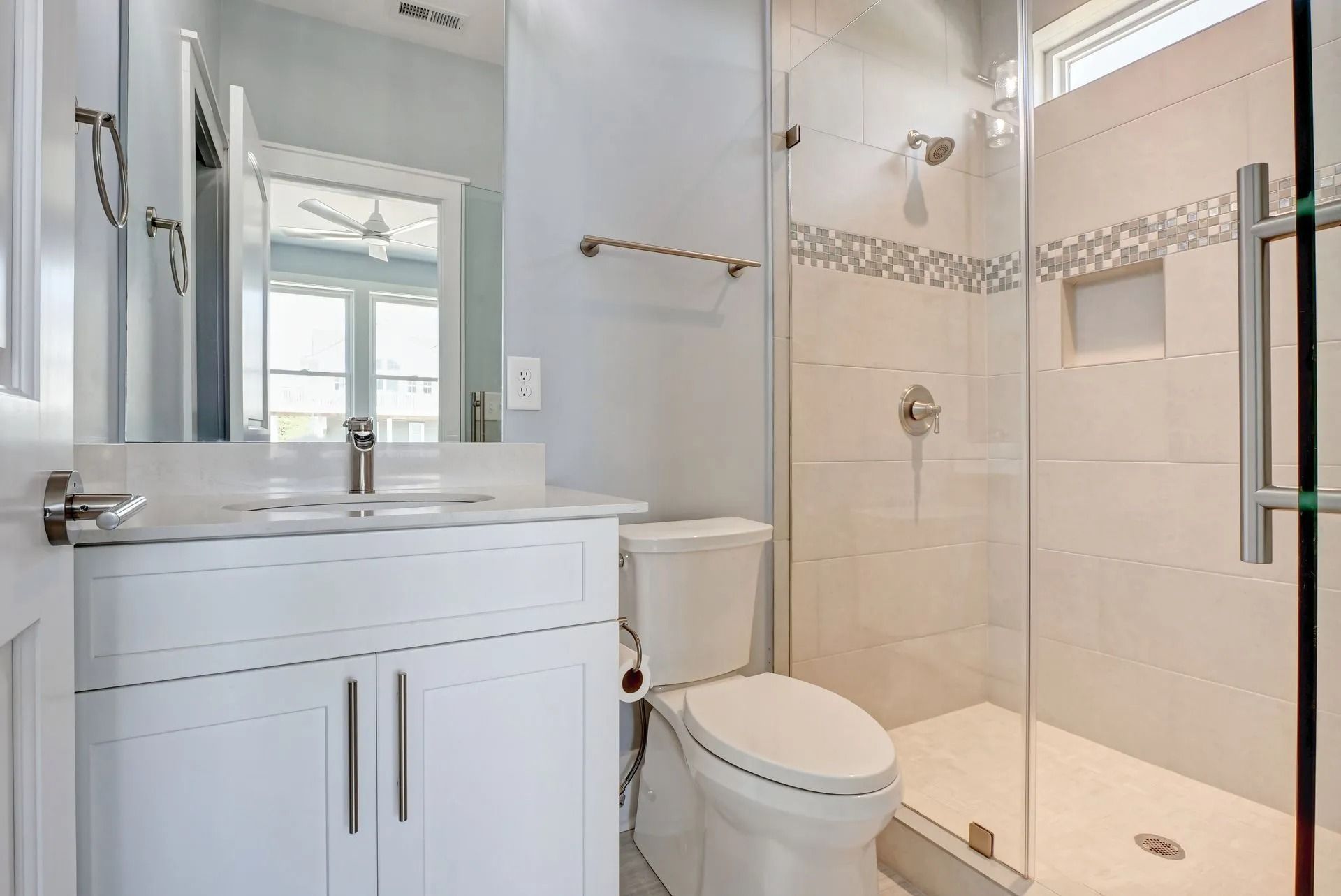Bathroom with white cabinets, toilet, and glass shower door; light blue walls.