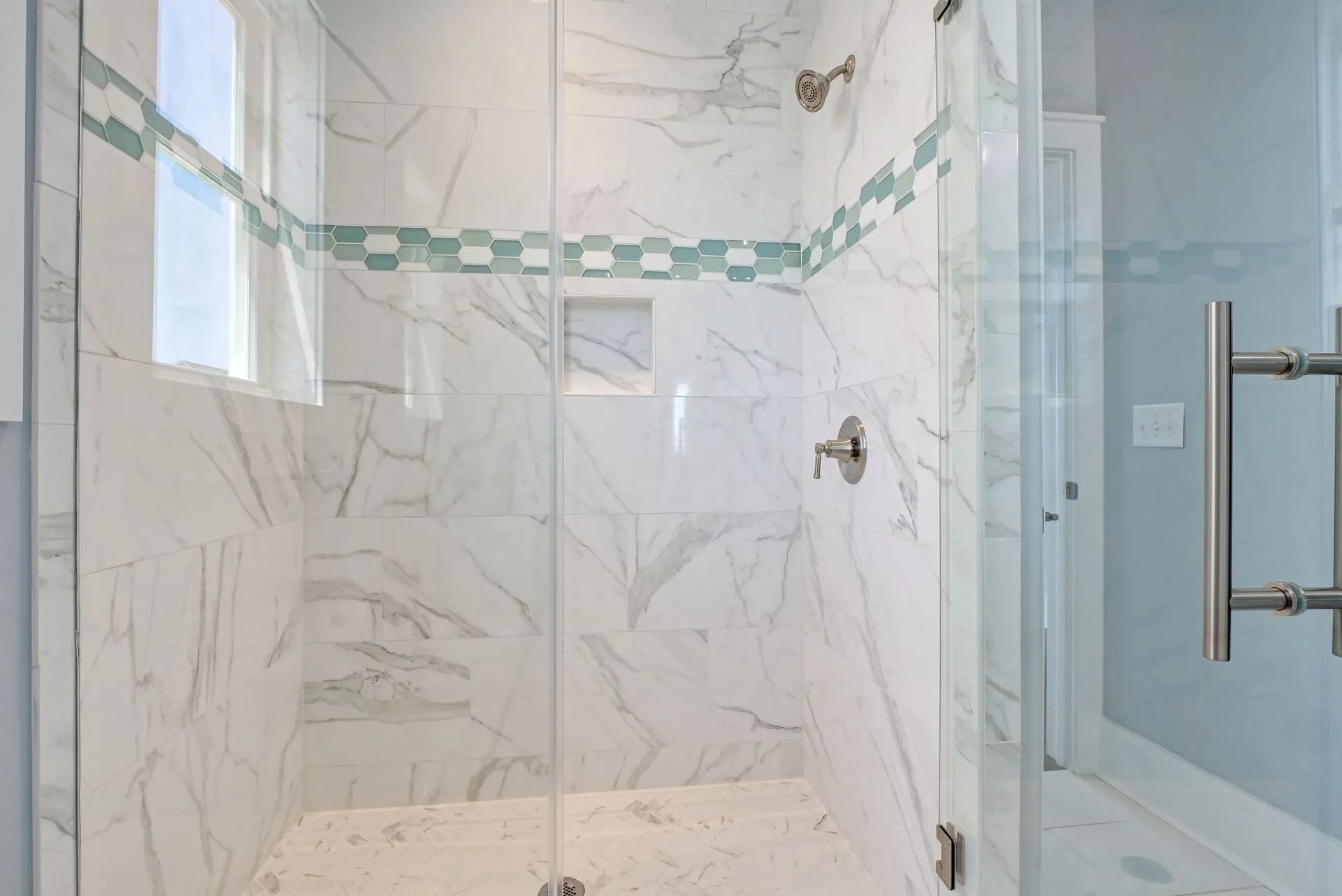 Glass-enclosed shower with white marble-look tiles. A row of blue tiles decorates the top.
