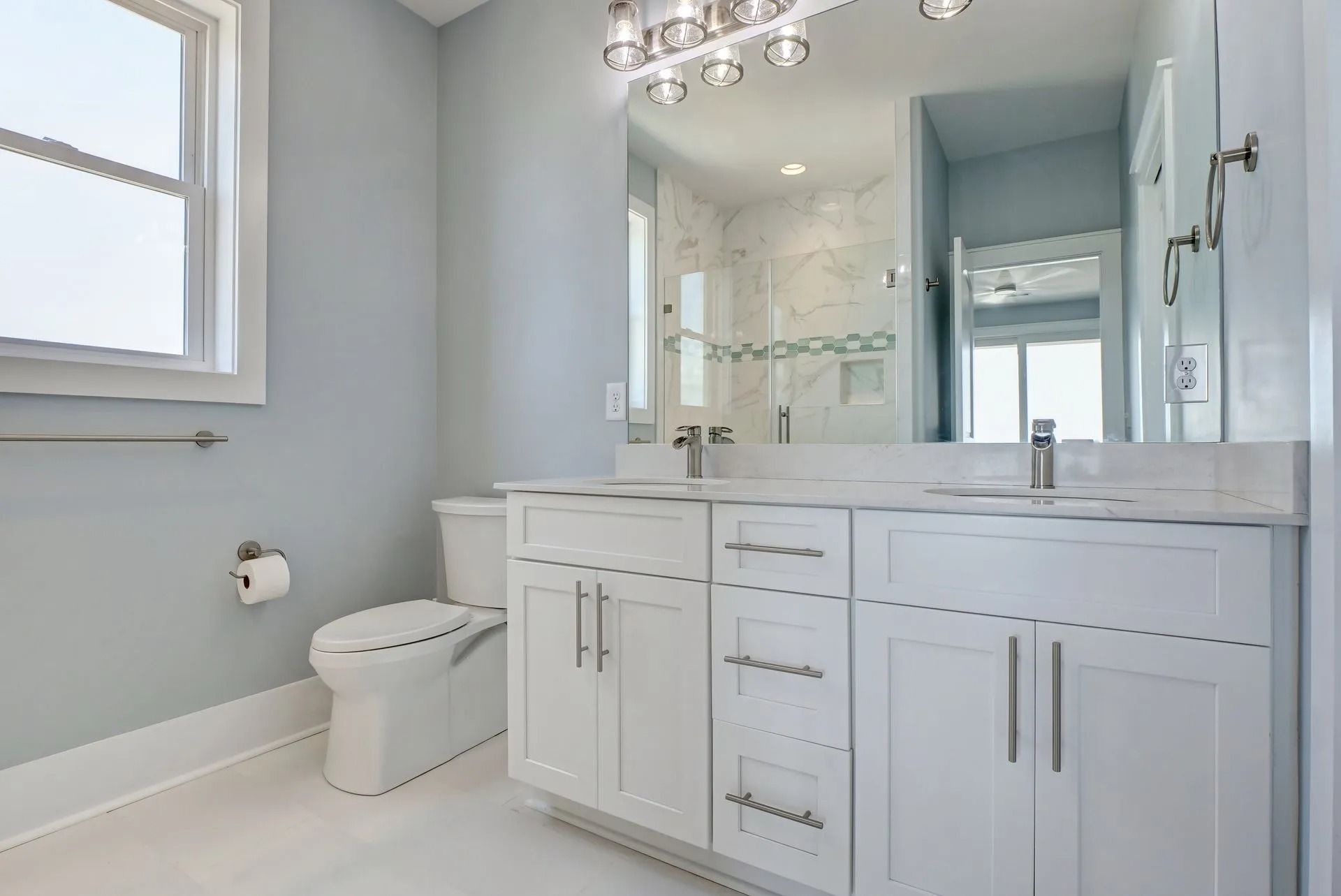 Light blue bathroom with white vanity, toilet, and window.
