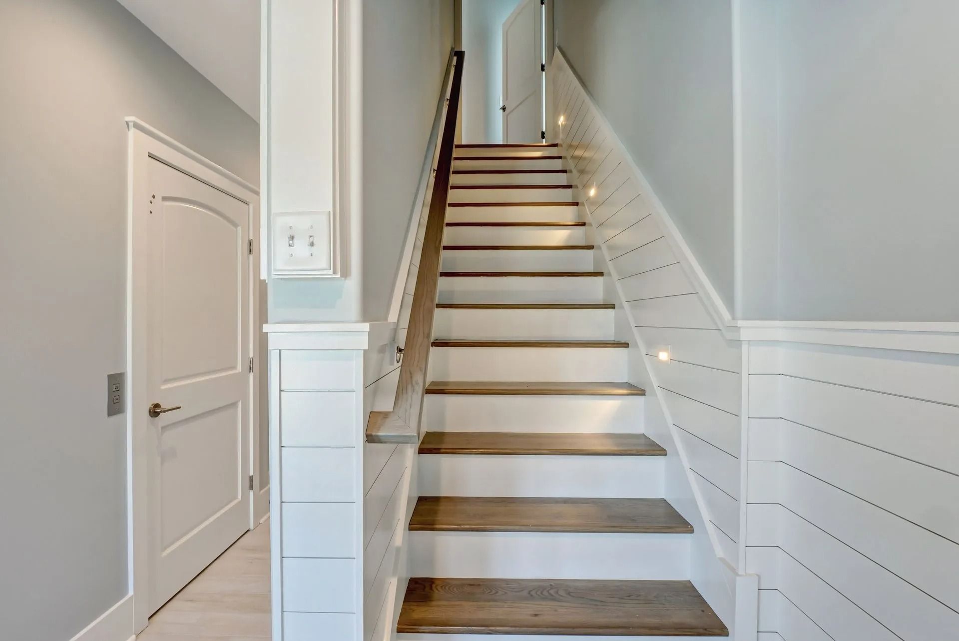 Staircase with wooden steps and white trim leading upwards; door on the left.
