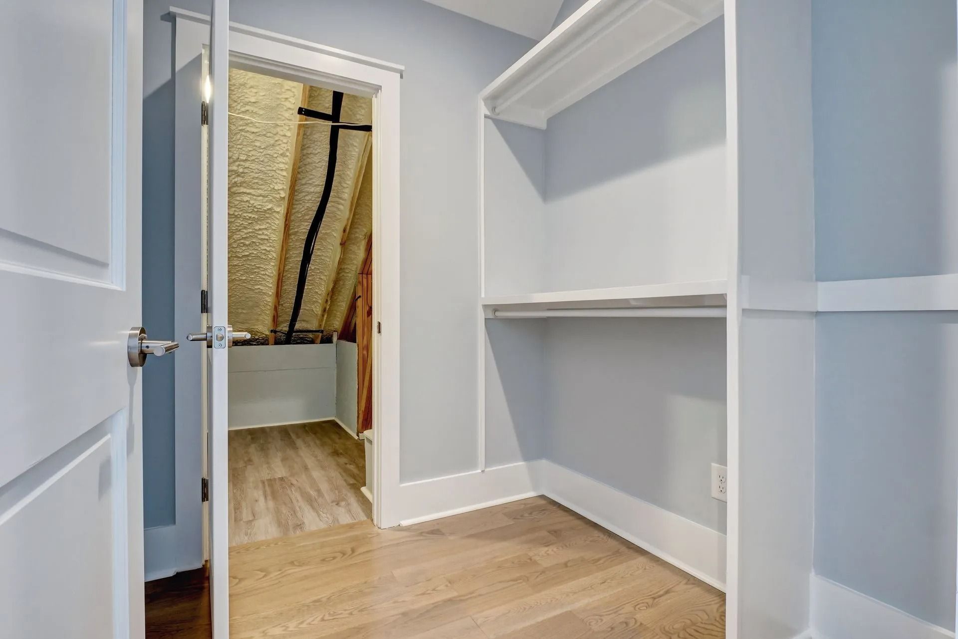 Empty closet with light blue walls, built-in shelves, and open door to attic storage.