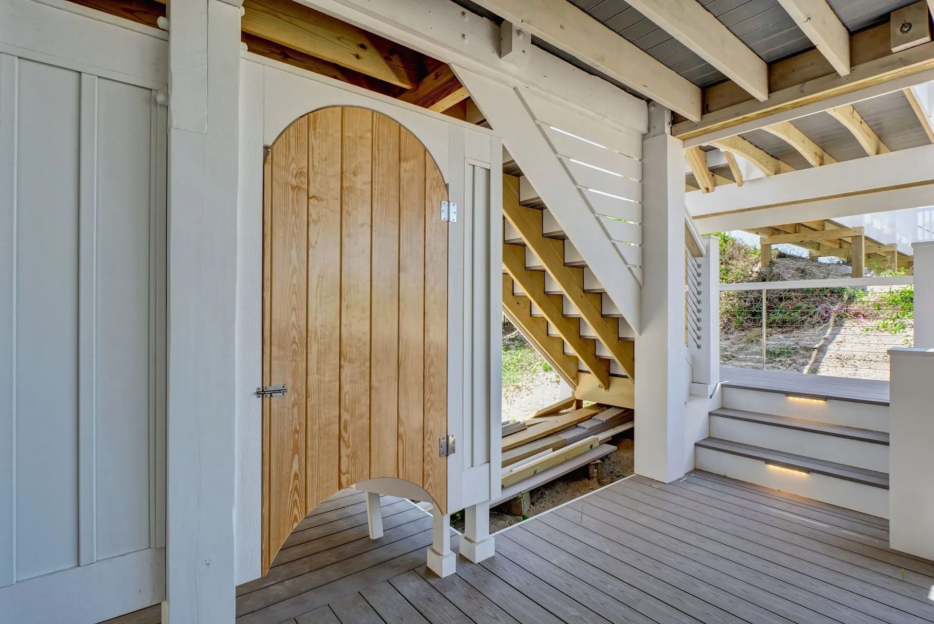 Wooden outdoor shower with a white trim, under a wooden deck, and adjacent stairs.