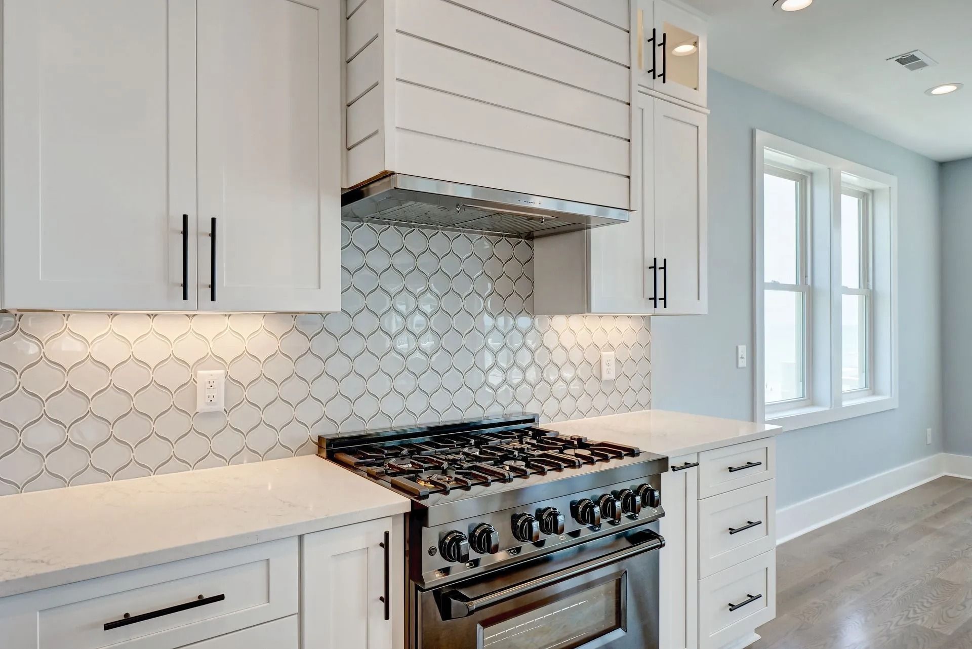 White kitchen with a stainless steel range and patterned backsplash.