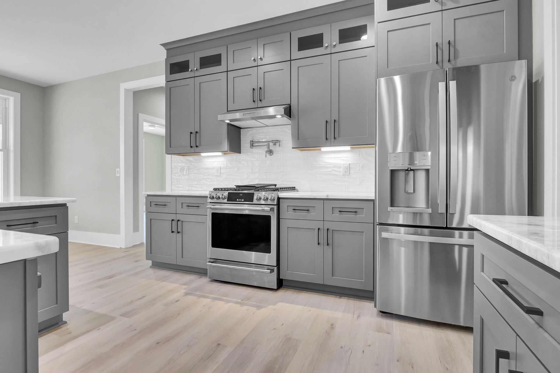 Gray kitchen with stainless steel appliances, light wood floors, and white countertops.