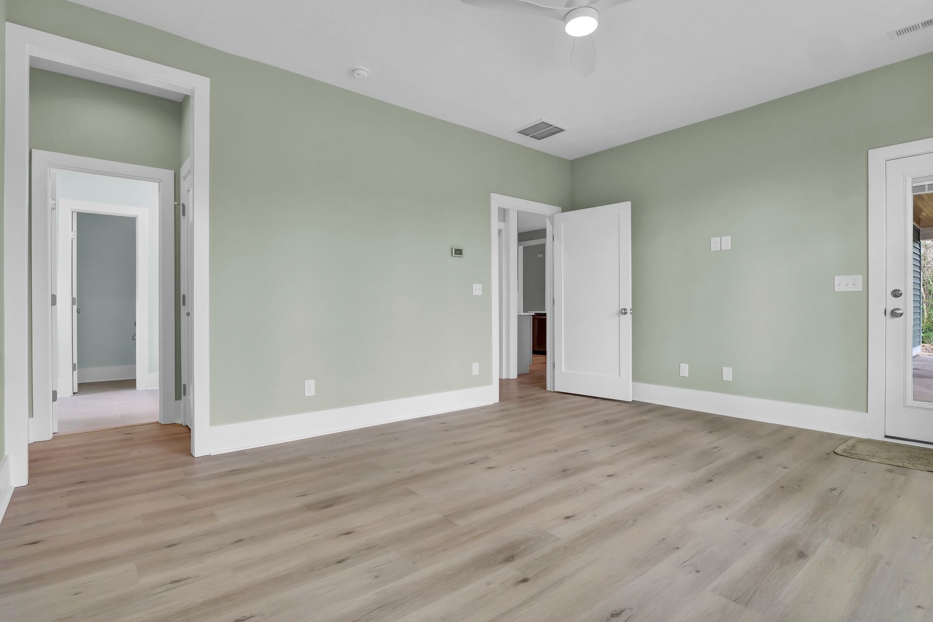 Empty room with light wood flooring, green walls, and white trim.