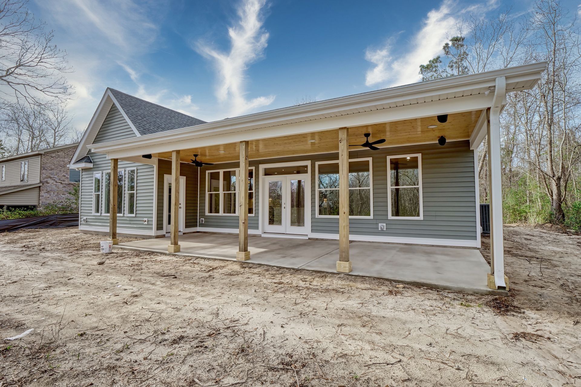 Back of a new house with a covered patio. Light blue siding, concrete patio, and white trim. Blue sky.