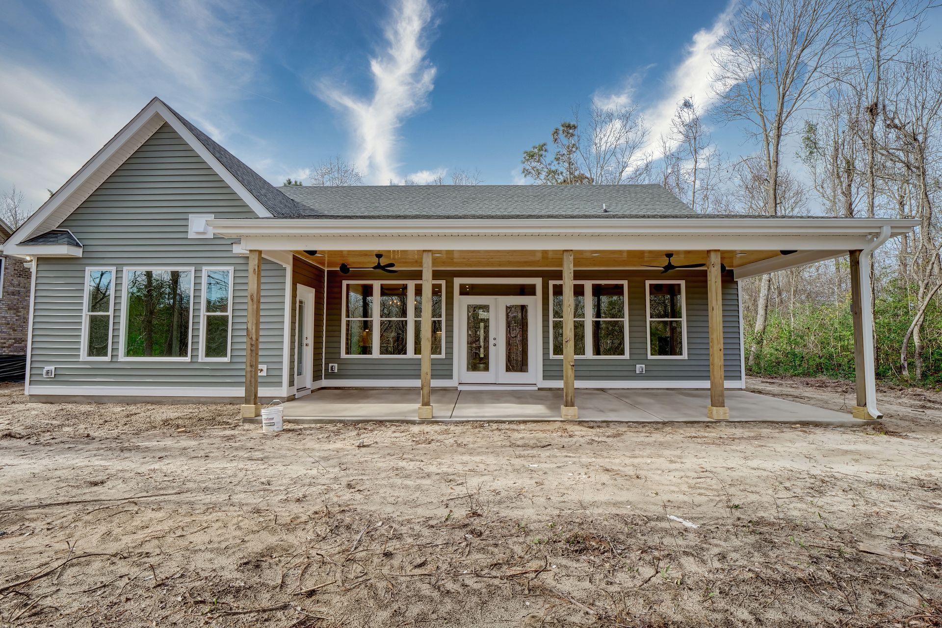 Light blue house with a covered porch on a cloudy day; unfinished dirt yard.