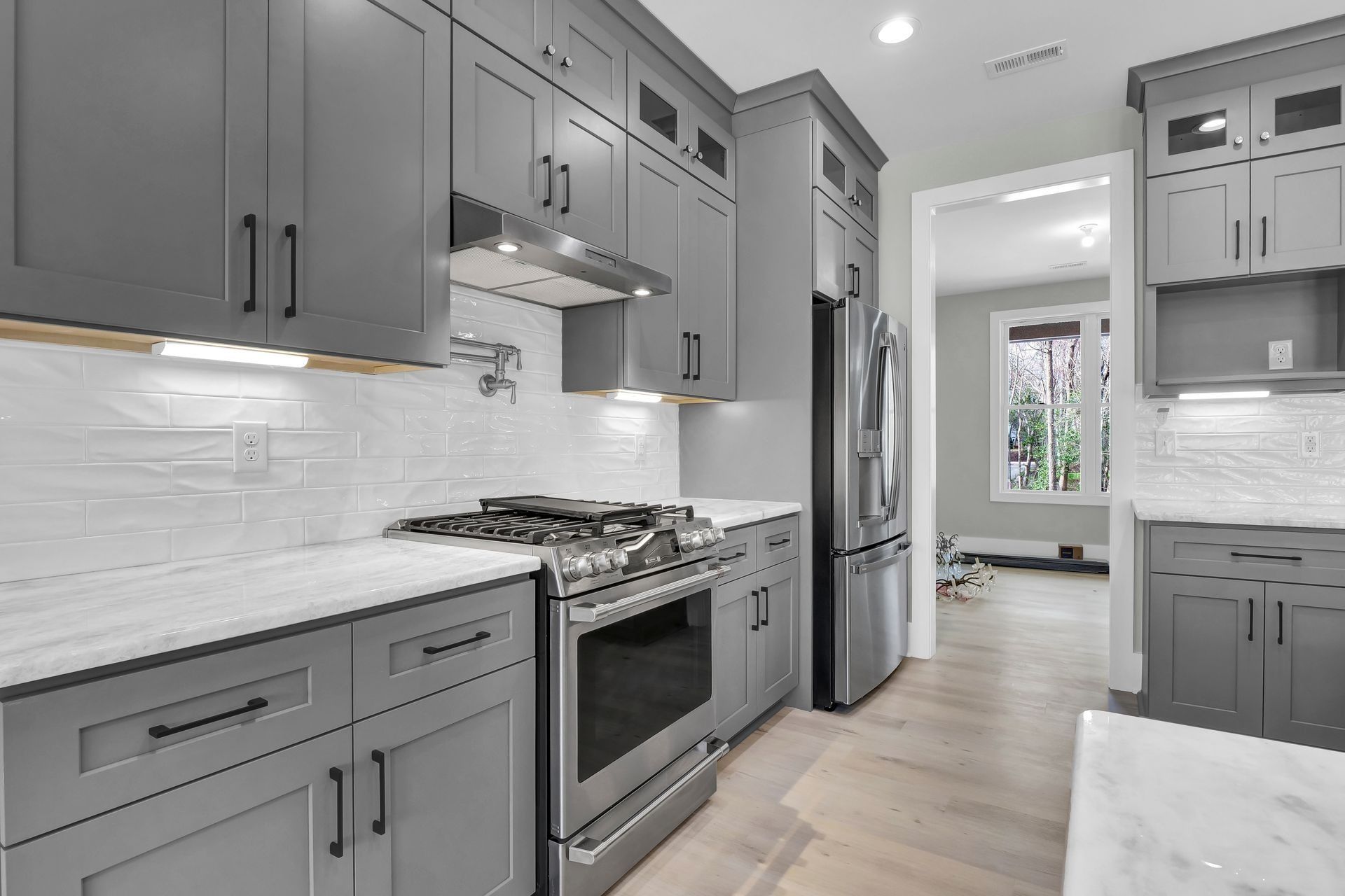 Gray kitchen cabinets, stainless steel appliances, marble countertops, white backsplash.
