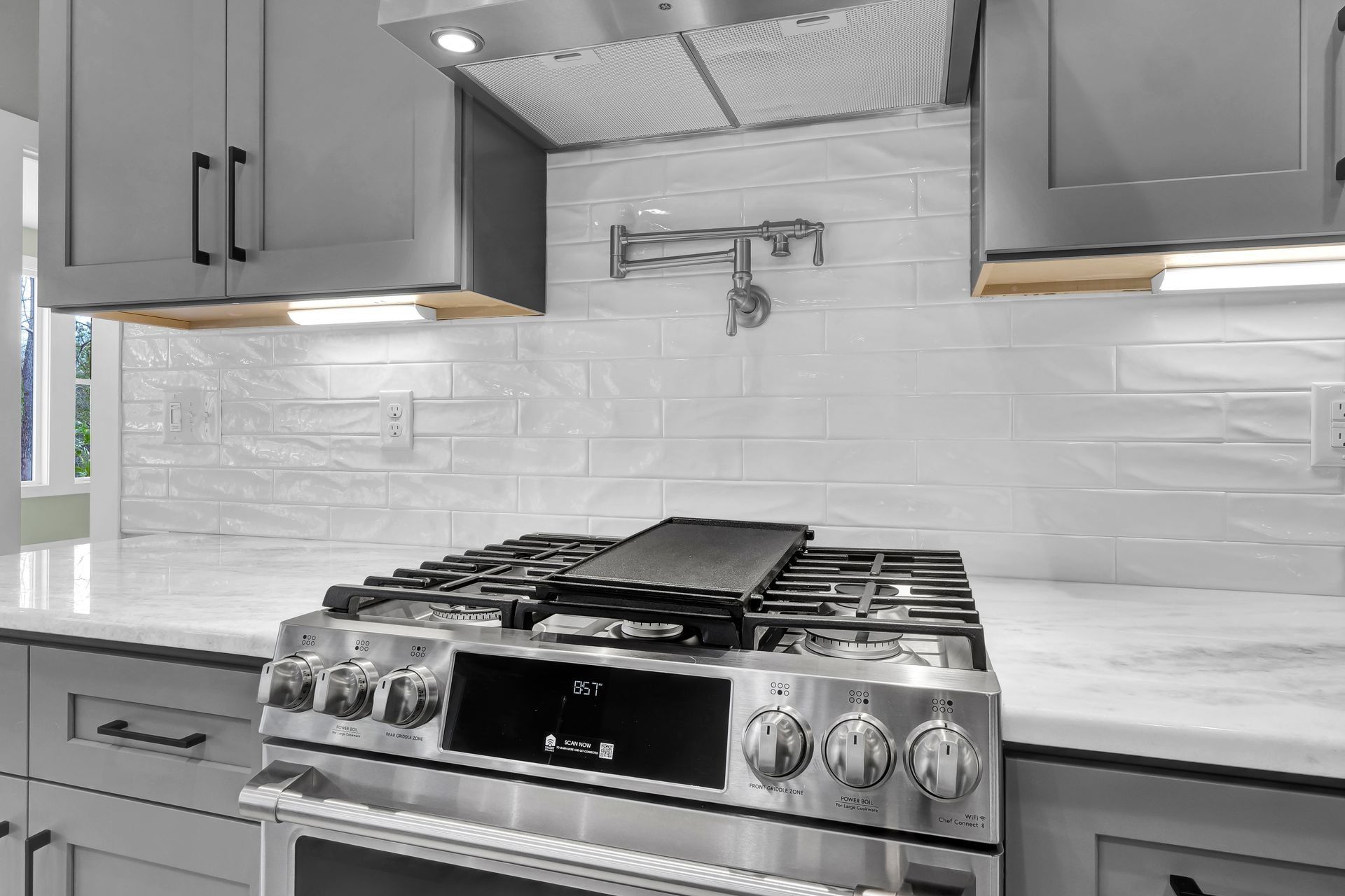 Modern kitchen with stainless steel stove, gray cabinets, white backsplash, and a pot filler.