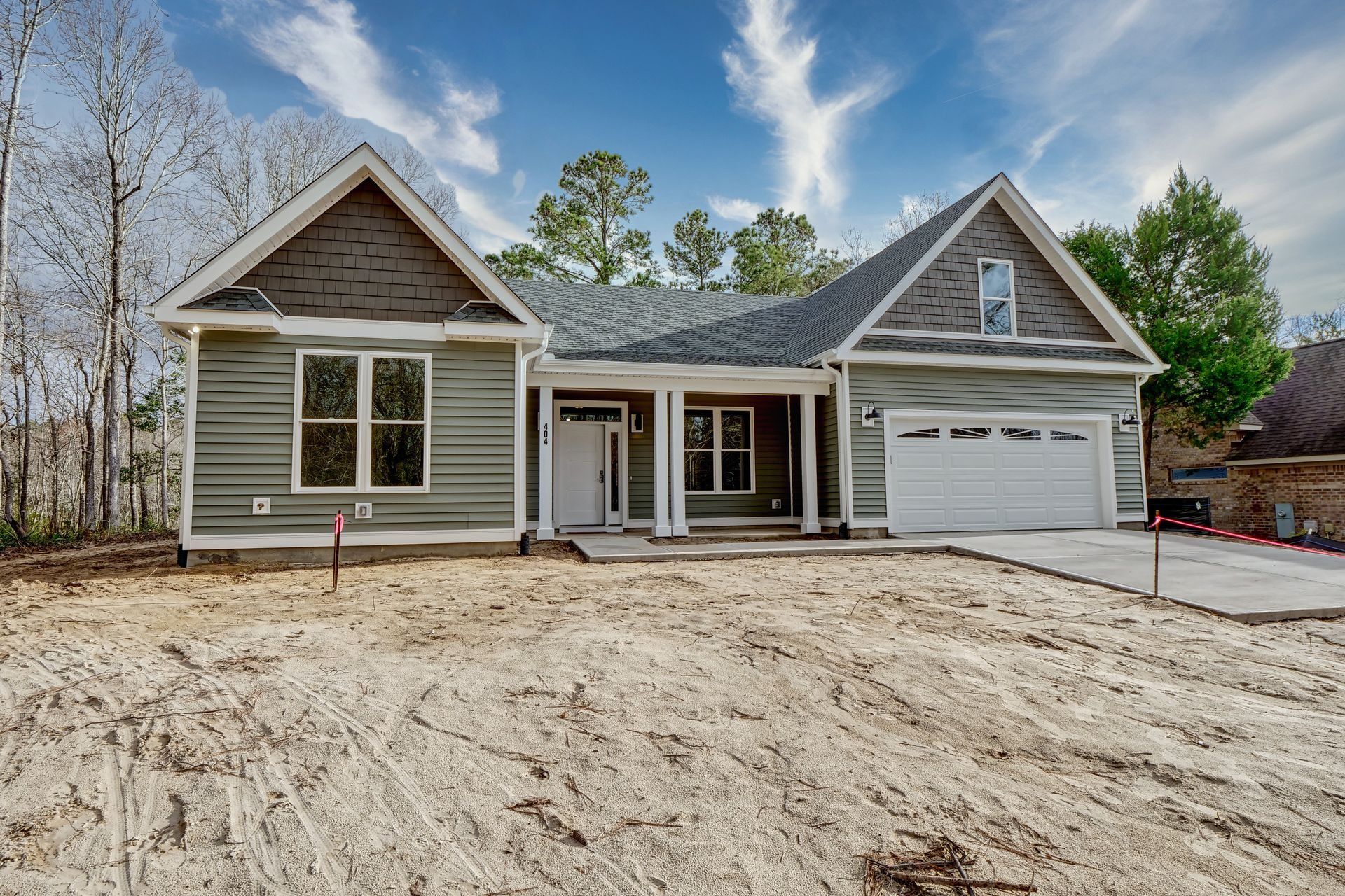 New construction house, green siding, gray roof, white garage door, sandy yard, blue sky.