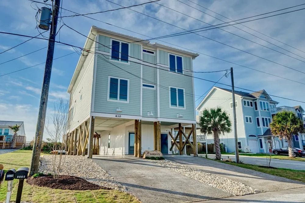 Two-story house with light blue siding on stilts; gravel driveway.