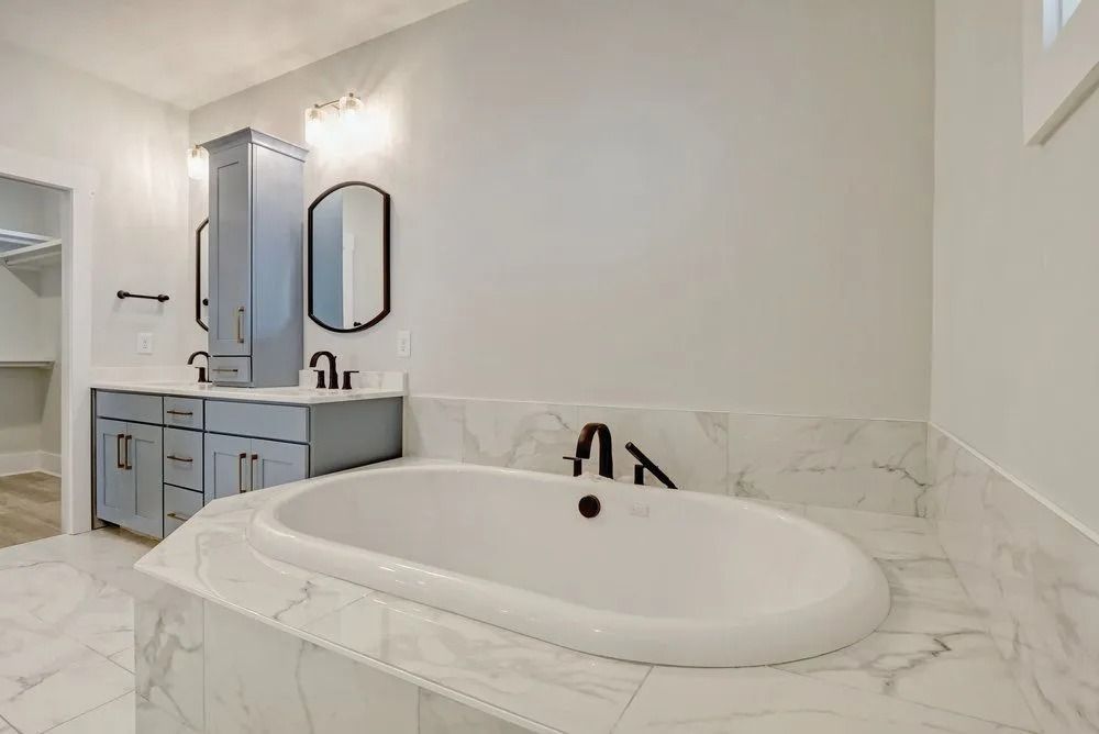 Modern bathroom with a white oval bathtub, blue vanity, and marble tile.