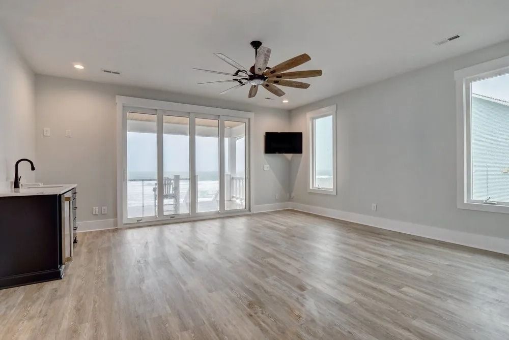 Empty modern room with wooden floor, folding glass doors, and a wet bar.