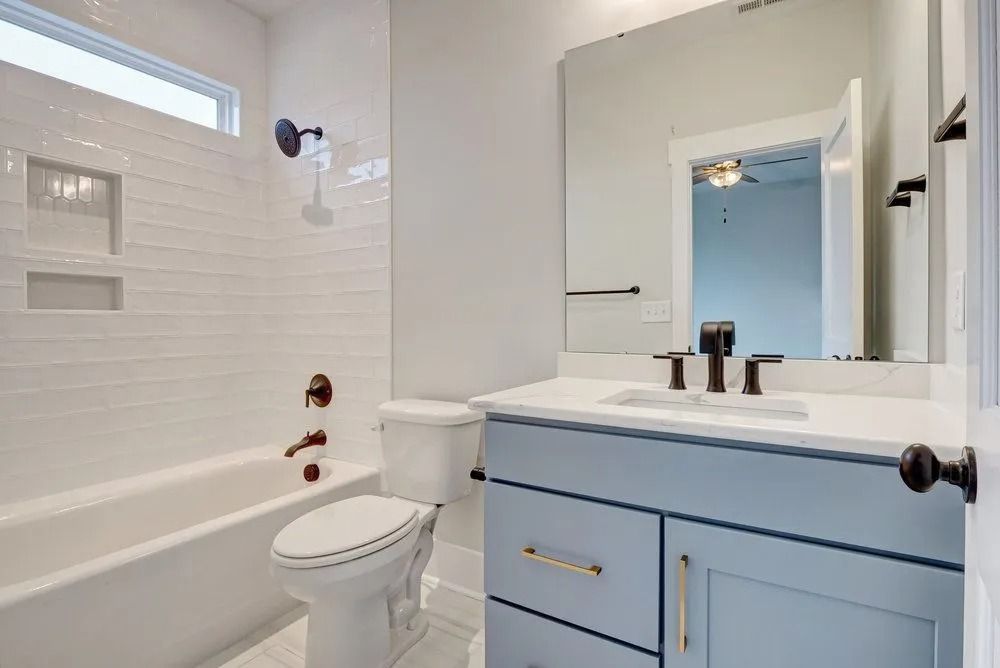 Bathroom with blue vanity, white walls, and a bathtub. Black fixtures.