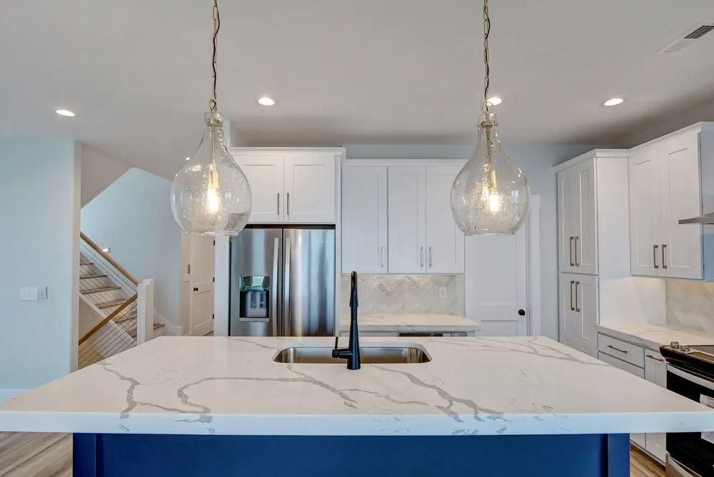 Modern kitchen with a white quartz island, blue cabinet base, and two glass pendant lights.