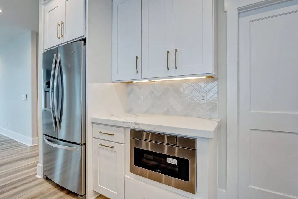 Kitchen with white cabinets, stainless steel refrigerator and microwave, and white backsplash.