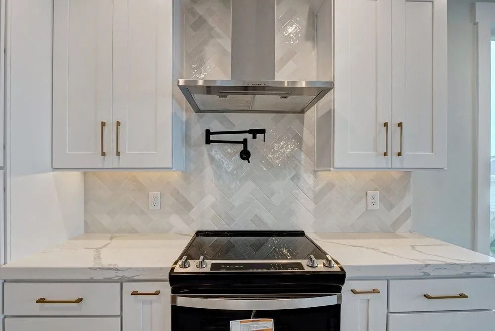 White kitchen with stainless steel appliances, marble backsplash, and white cabinets with gold handles.