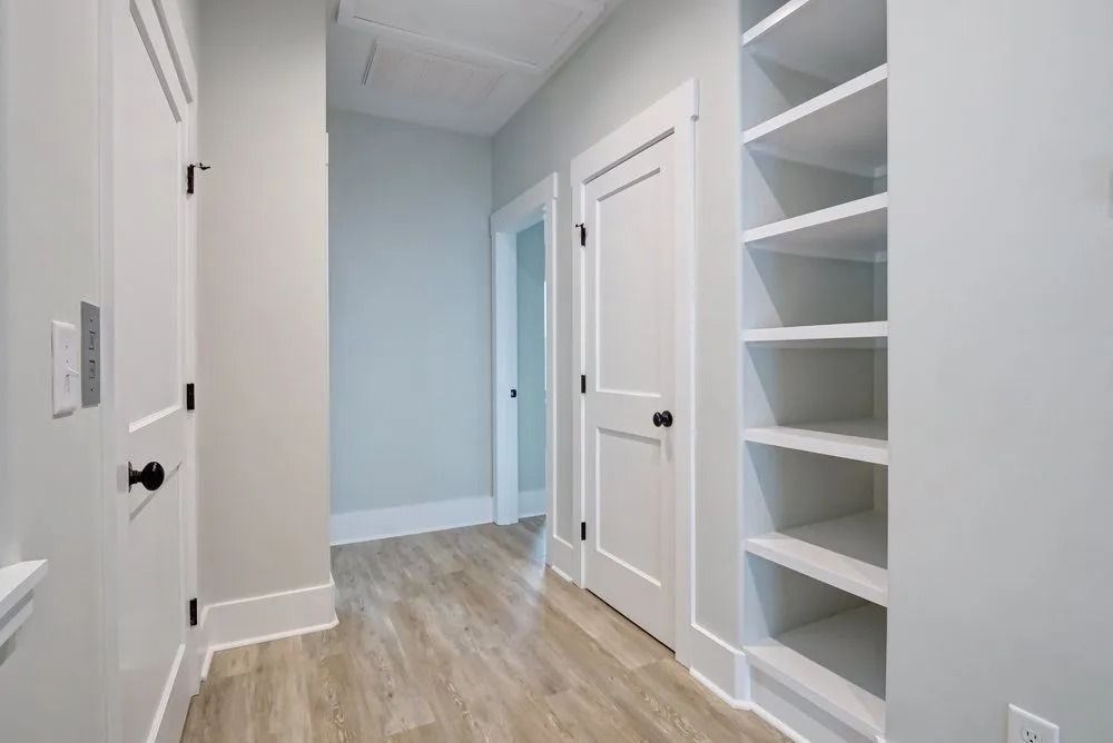 Narrow hallway with white doors, built-in shelves, and light wood-look flooring.