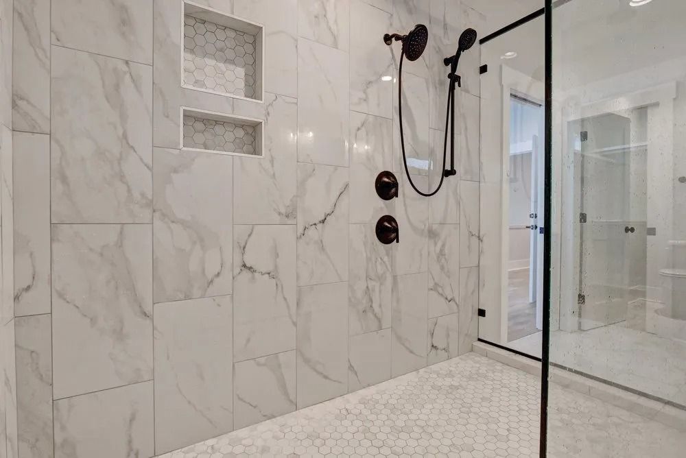White marble tile shower with black fixtures; glass door; two built-in niches.