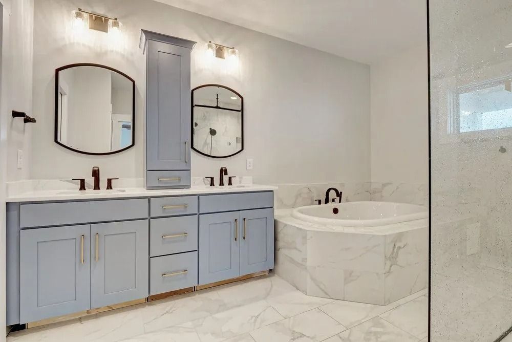 Bathroom with light blue vanity, black-framed mirrors, and a marble-tiled tub.